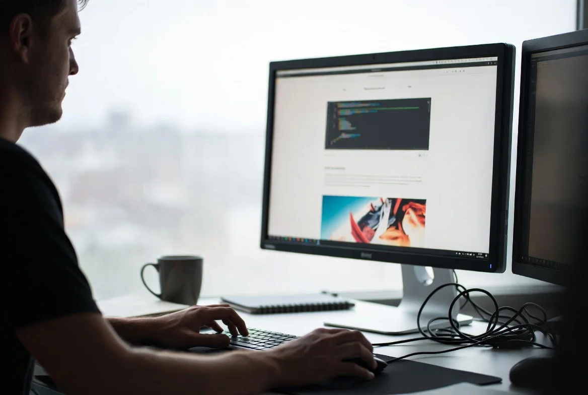 Our web developer working on a dual-monitor setup, writing clean code for a modern website interface and UI/UX design.